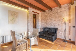 Une pièce avec un mur en pierre, une table en verre avec des chaises, un canapé en cuir noir et un lampadaire.