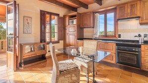 A kitchen with wooden cabinets, a glass dining table, wicker chairs, and a built-in oven. - Apartment 'Es turo de Formentera' with Pool, A/C and Wi-Fi (Ses Salines)