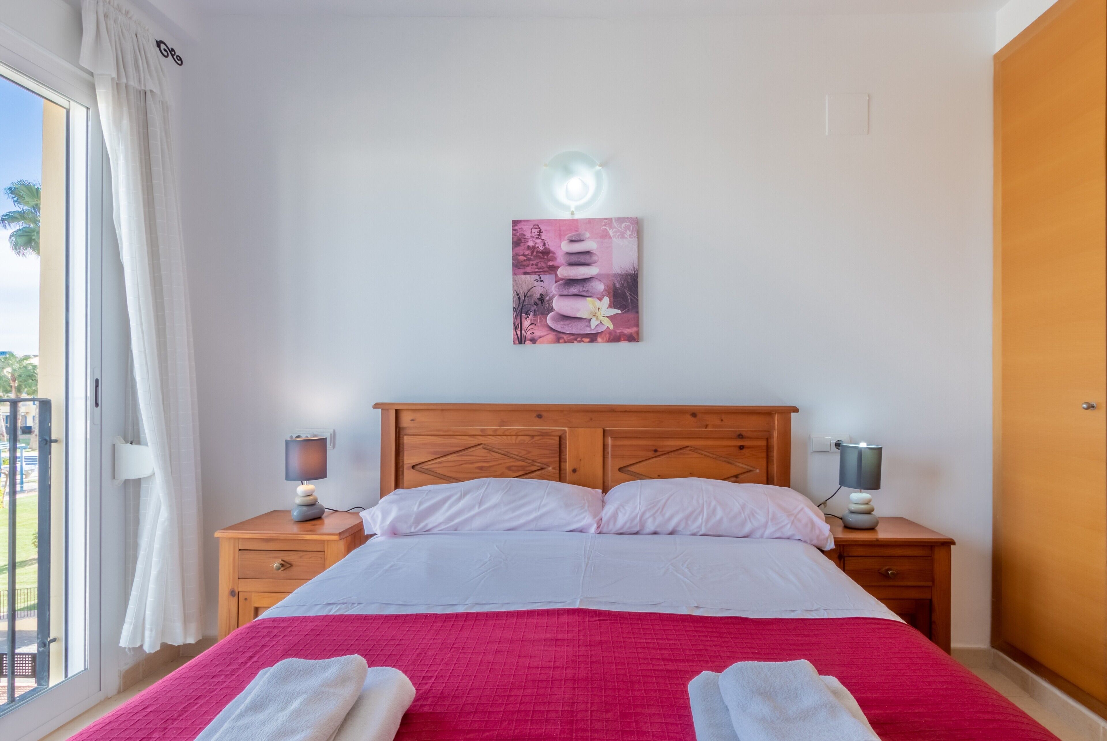 Un dormitorio con una cama, dos mesitas de noche, un armario auxiliar, una ventana con cortinas y una obra de arte colgada en la pared.