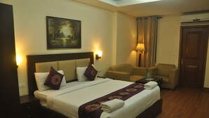A hotel room with a large bed, two bedside lamps, a painting on the wall, a chair, and a door. - Lohmod Hotel (New Delhi)