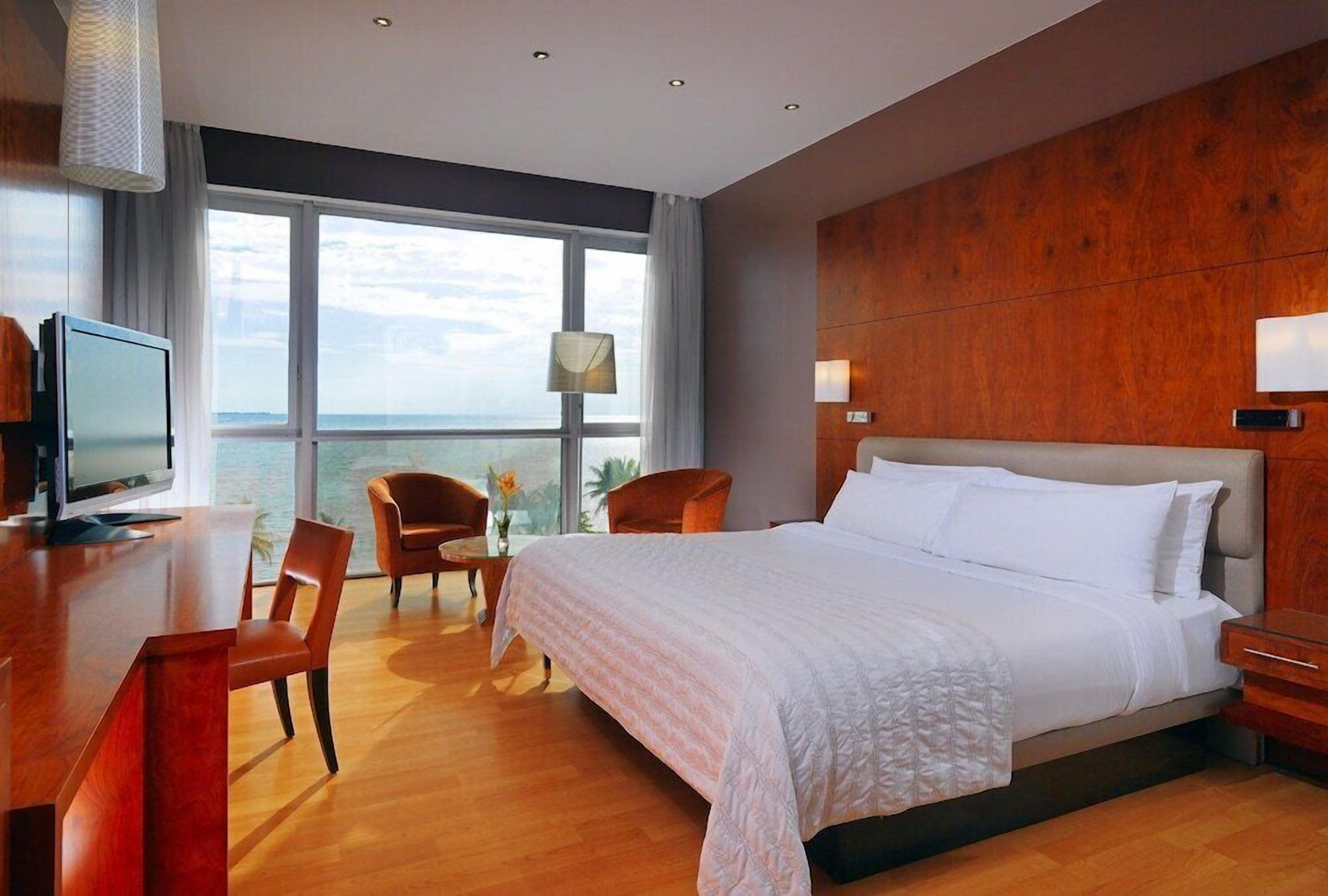 Une chambre d’hôtel avec un grand lit, un bureau avec une télévision et une vue sur l’océan.