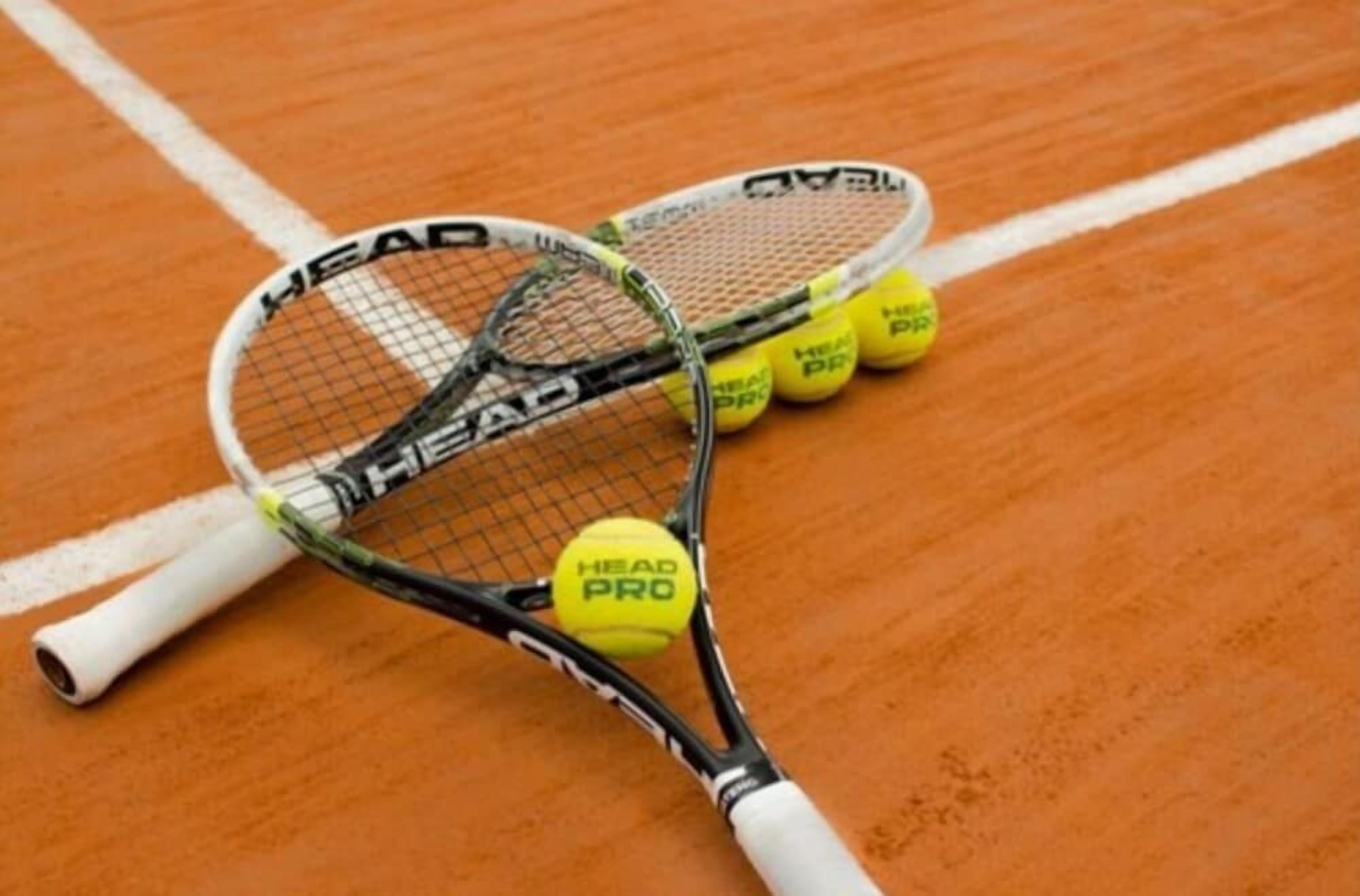 Two tennis rackets and three tennis balls on a clay court.
