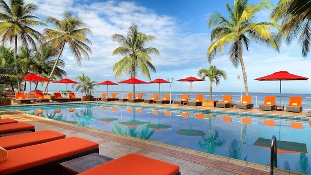 A poolside area with lounge chairs and umbrellas, palm trees, and a view of the ocean. - Le Meridien Re-ndama (Libreville)