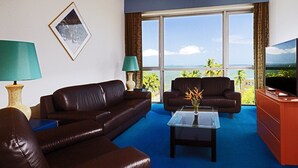 A living room with a brown leather sofa, a glass coffee table, and a television on a stand. - Le Meridien Re-ndama (Libreville)