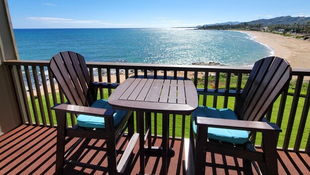 A wooden deck with two chairs and a table overlooking a beach with clear blue water and a distant shoreline. - WOW! AMAZING OCEANFRONT CONDO 2nd Floor STUNNING VIEWS, GREAT LOCATION IN KAUAI (Kapaʻa)
