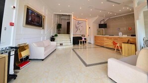 Un amplio vestíbulo con mostrador de recepción, una escalera y un área de descanso.