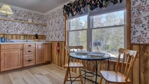 Una cocina con armarios de madera, una mesa redonda de vidrio y sillas. Hay una ventana con vistas a árboles y un extintor en la pared.