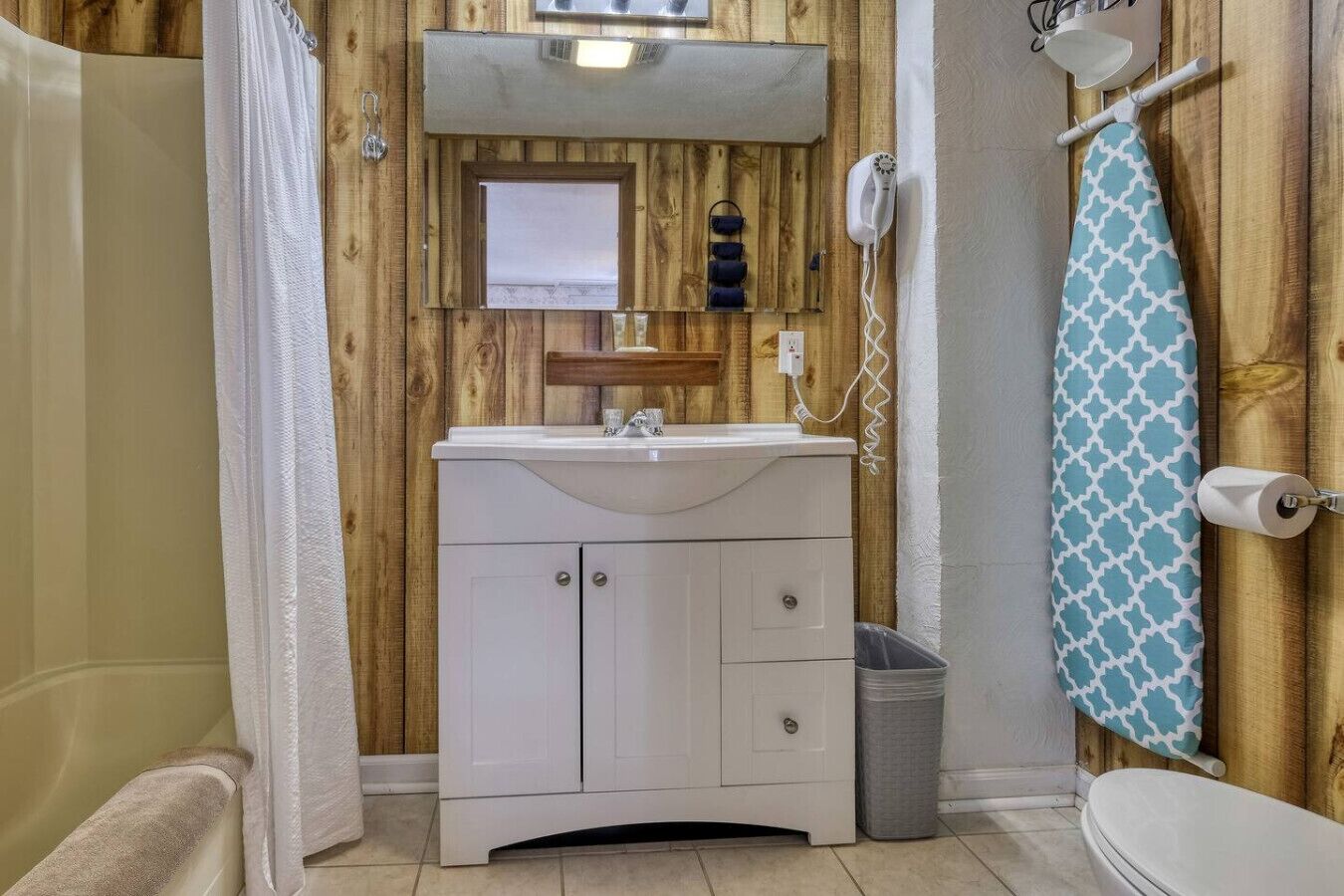 Une salle de bain avec un mur en bois, un lavabo blanc, un miroir, un téléphone et un porte-serviettes.