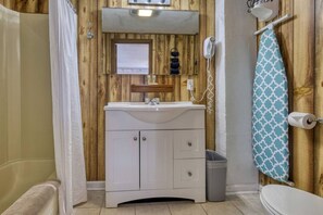 Une salle de bain avec un mur en bois, un lavabo blanc, un miroir, un téléphone et un porte-serviettes.