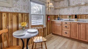 Una cocina con armarios de madera, una mesa redonda con sillas, un ventanal con vistas a una terraza nevada y una lámpara fijada a la pared.