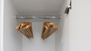 Un dressing avec une porte, un coffre-fort noir, des cintres en bois et une tringle à rideaux en métal.