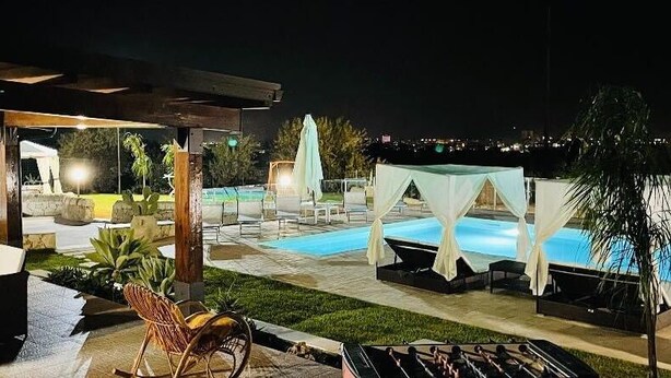 An outdoor pool area with lounge chairs and umbrellas, a covered seating area, and a view of the city at night.
