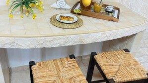 A kitchen counter with a potted plant, a fruit pitcher, and a tray with a plate of food. There are two woven stools in front of the counter.