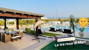 An outdoor pool area with lounge chairs, a table, and a covered seating area.