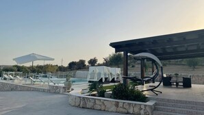 A poolside area with lounge chairs, a covered seating area, and a view of the landscape.