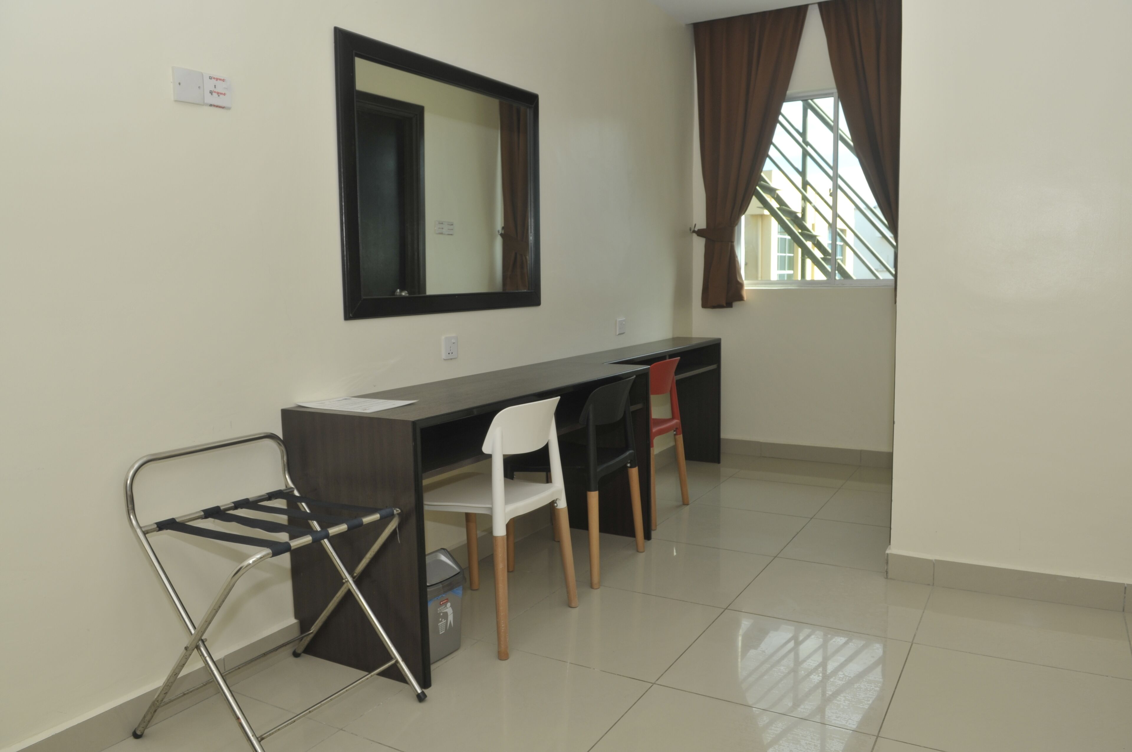 A room with a desk, chairs, a mirror, a window with curtains, and a radiator.