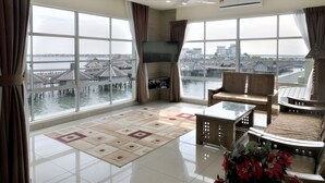 Ein geräumiges Zimmer mit großen Fenstern, einem Deckenventilator und Blick auf das Wasser.