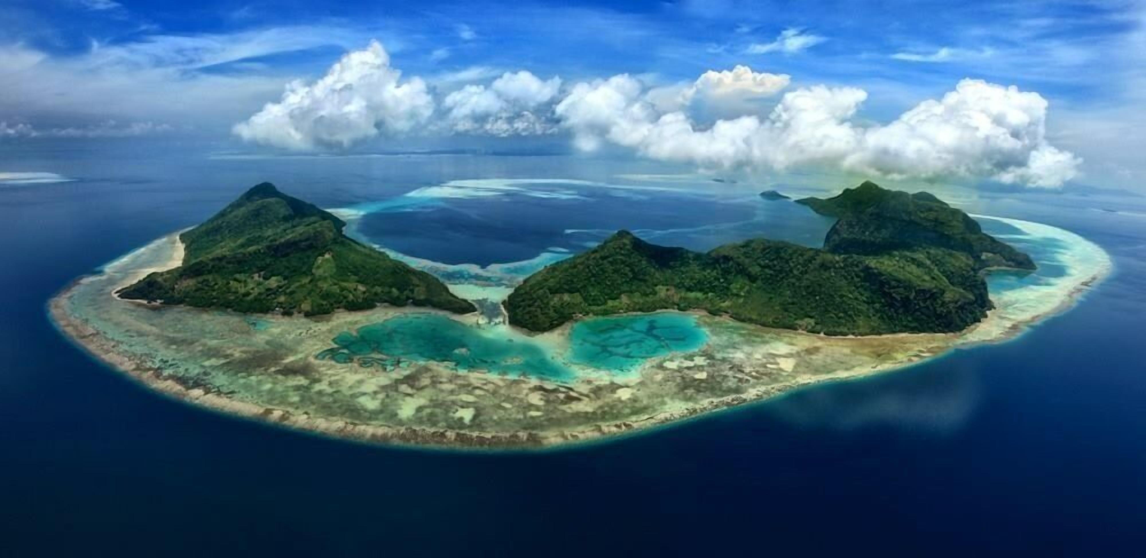 Vista aérea de una isla tropical con tres montañas verdes destacadas y aguas azules cristalinas que la rodean.