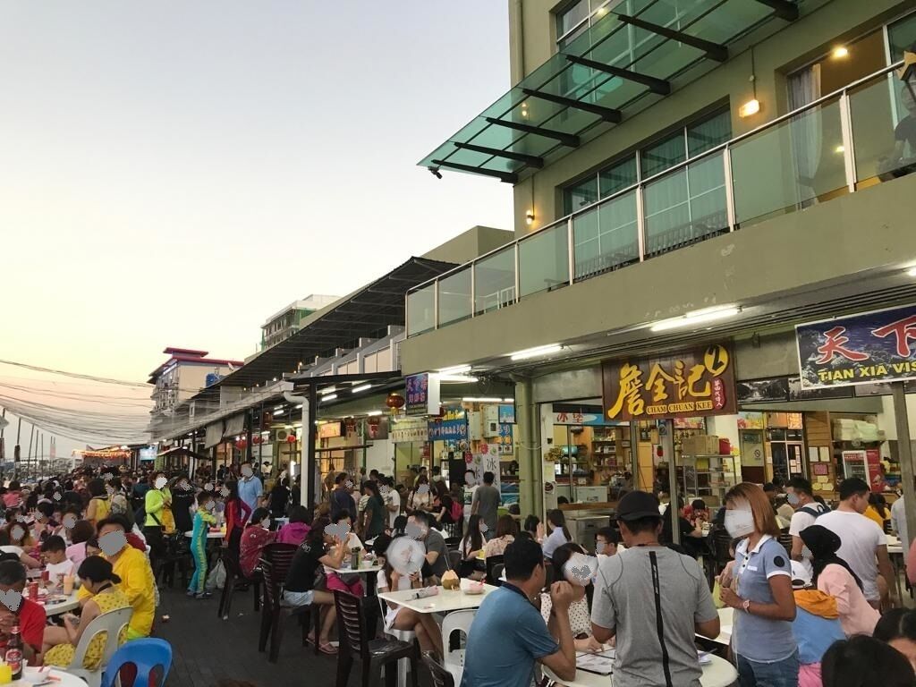 Un espacio al aire libre concurrido para comer, con varias mesas y sillas, rodeado de puestos de comida y restaurantes.
