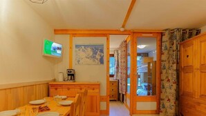 A cozy room with a wooden dining table set for two, a coffee machine, and a painting on the wall. - Ski-In/Ski-Out Apartment in Val Thorens - 6 Guests, Comfort Features, Central Location (Val Thorens)