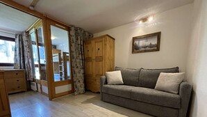 A cozy living room with a grey sofa, wooden cabinets, and a large window with curtains. - Ski-In/Ski-Out Apartment in Val Thorens - 6 Guests, Comfort Features, Central Location (Val Thorens)