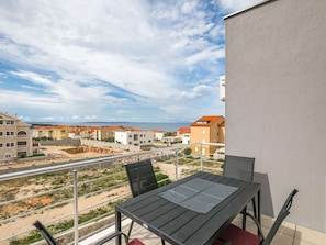 Uma varanda com mesa e cadeiras, com vista para uma área residencial com diversos edifícios e céu claro.