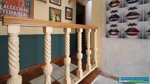A staircase with a wooden handrail and white balusters, leading to a room with a tiled floor and a wall decorated with framed pictures and a poster. - Immaculate House in Montejaque Sleeps 6 (Montejaque)