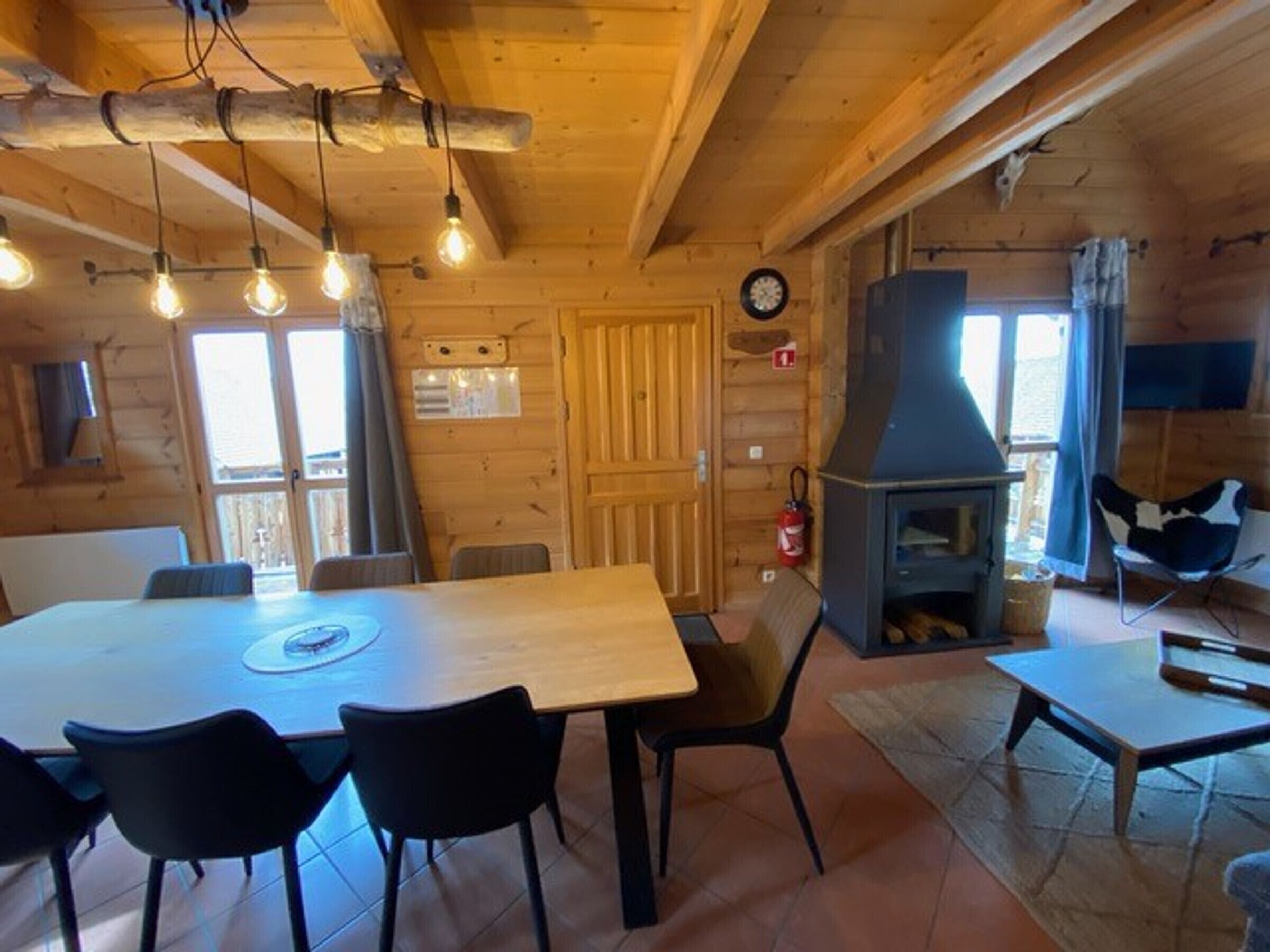L’intérieur d’un chalet en bois comprend une table à manger, des chaises, une cheminée et une horloge murale.