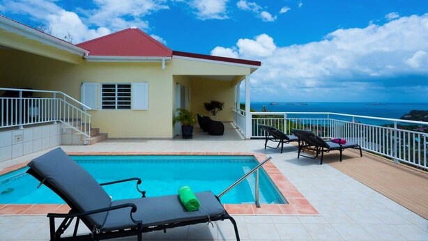 Un área junto a la piscina con sillones de descanso, una casita con tejado rojo y vista al océano.