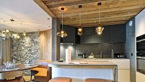 A modern kitchen with a stone wall, wooden ceiling, and pendant lights.