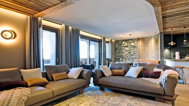A modern living room with two sofas, a stone accent wall, and a kitchen area visible through an open door.