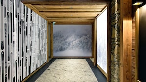 A hallway with a wooden ceiling, a stone wall, and a large window with a snowy forest view.