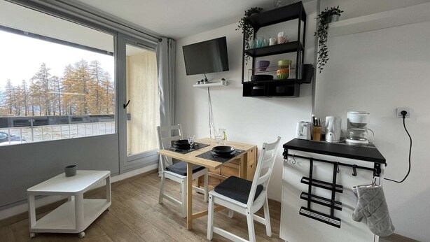 Une cuisine moderne avec un coin repas, un téléviseur fixé au mur et une vue sur l’extérieur.