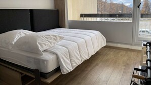 Une chambre d’hôtel moderne avec un lit, une vue sur un parking et un balcon doté d’une rambarde.