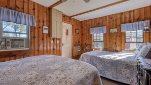 Een chalet met twee bedden, houten wanden, een plafondventilator en een raam met uitzicht.