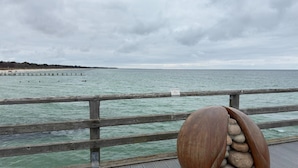 En træbrygge med gelænder, en klippeformation og en fjer beliggende kystlinje.