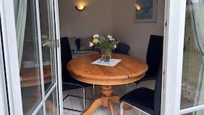 Et rundt træbord med en vase blomster, sorte stole og en vægmonteret lampe.