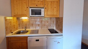 A compact kitchen with wooden cabinets, a microwave, a sink, a dishwasher, and a refrigerator. - Studio at the slopes with balcony, parking, 4 people (Les Deux Alpes)