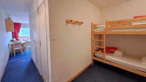 A room with bunk beds, a wooden table with chairs, a red curtain, and a ceiling light fixture. - Studio at the slopes with balcony, parking, 4 people (Les Deux Alpes)