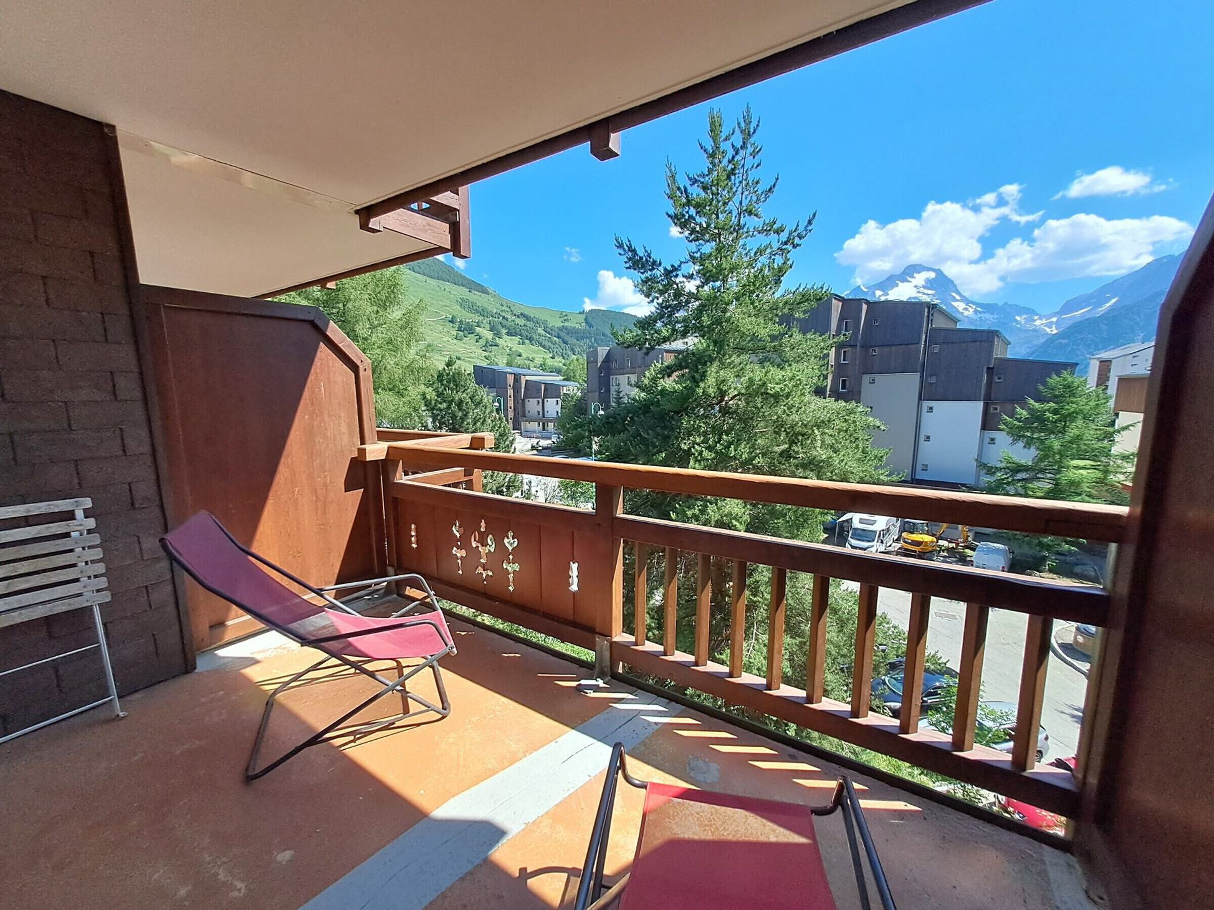 Ein Balkon mit Blick auf eine Berglandschaft, ein roter Stuhl und ein Holgitter.