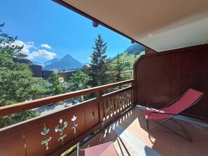 Un balcon avec une chaise rouge, une vue sur les montagnes et un ciel dégagé.