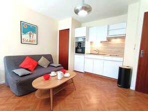 Un espacio habitable pequeño con un sofá, una mesa de comedor, una kitchenette y un cubo de basura.