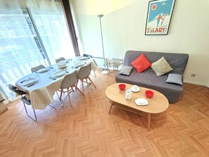 A dining area with a table set for four, a sofa with cushions, and a coffee table with cups and a plate.
