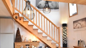 A dining area with a wooden table set for four, a staircase with wooden railings, and a wall-mounted light fixture. - Cozy chalet with mezzanine, wood stove, wifi and parking - Méribel (Méribel)