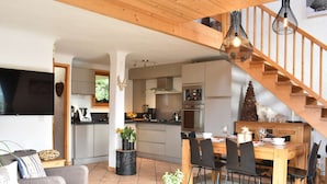 A modern kitchen with a dining area, wooden staircase, and a flat-screen TV. - Cozy chalet with mezzanine, wood stove, wifi and parking - Méribel (Méribel)