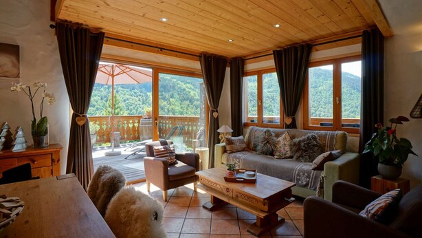 A cozy living room with a wooden ceiling, large windows with curtains, a sofa, a coffee table, and a view of a forested area. - Cozy chalet with mezzanine, wood stove, wifi and parking - Méribel (Méribel)