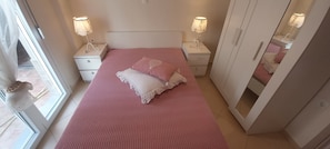 A bedroom with a bed, two bedside tables with lamps, a wardrobe, and a window.