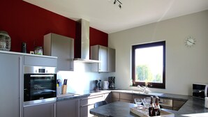 Eine moderne Küche mit Edelstahlgeräten, einem Essbereich mit Tisch und Stühlen sowie einem großen Fenster für natürliches Licht.