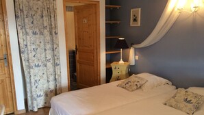 Un dormitorio con una cama, una mesita de noche, una lámpara, una puerta y una cortina.