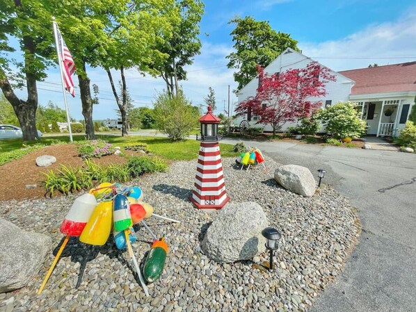 Ein Garten mit einem rot-weiß gestreiften Leuchtturm, bunten Bojen und einem weißen Gebäude mit rotem Dach.